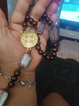 Cliente segurando o terço com medalha de São Bento na mão